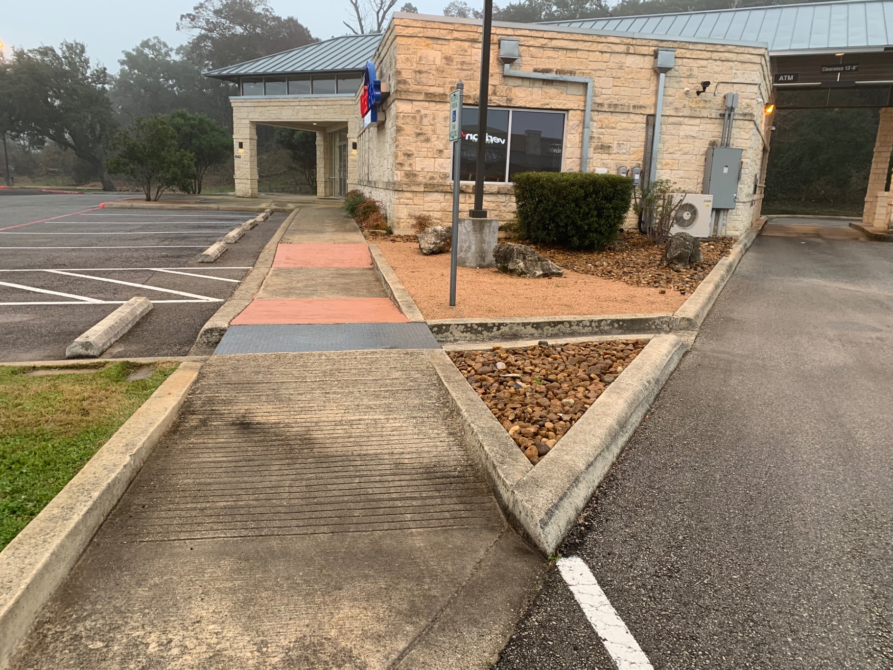 Side elevation of the credit union with the illuminated United Texas sign before cleaning, showing dark bands of buildup along the limestone