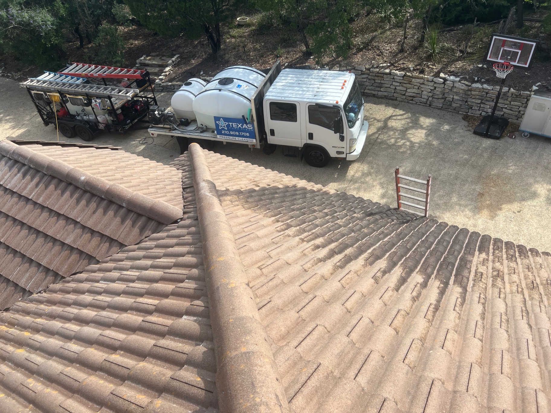 Tile roof during soft wash cleaning showing a sharp contrast between the clean treated section and the dark untreated algae-covered section