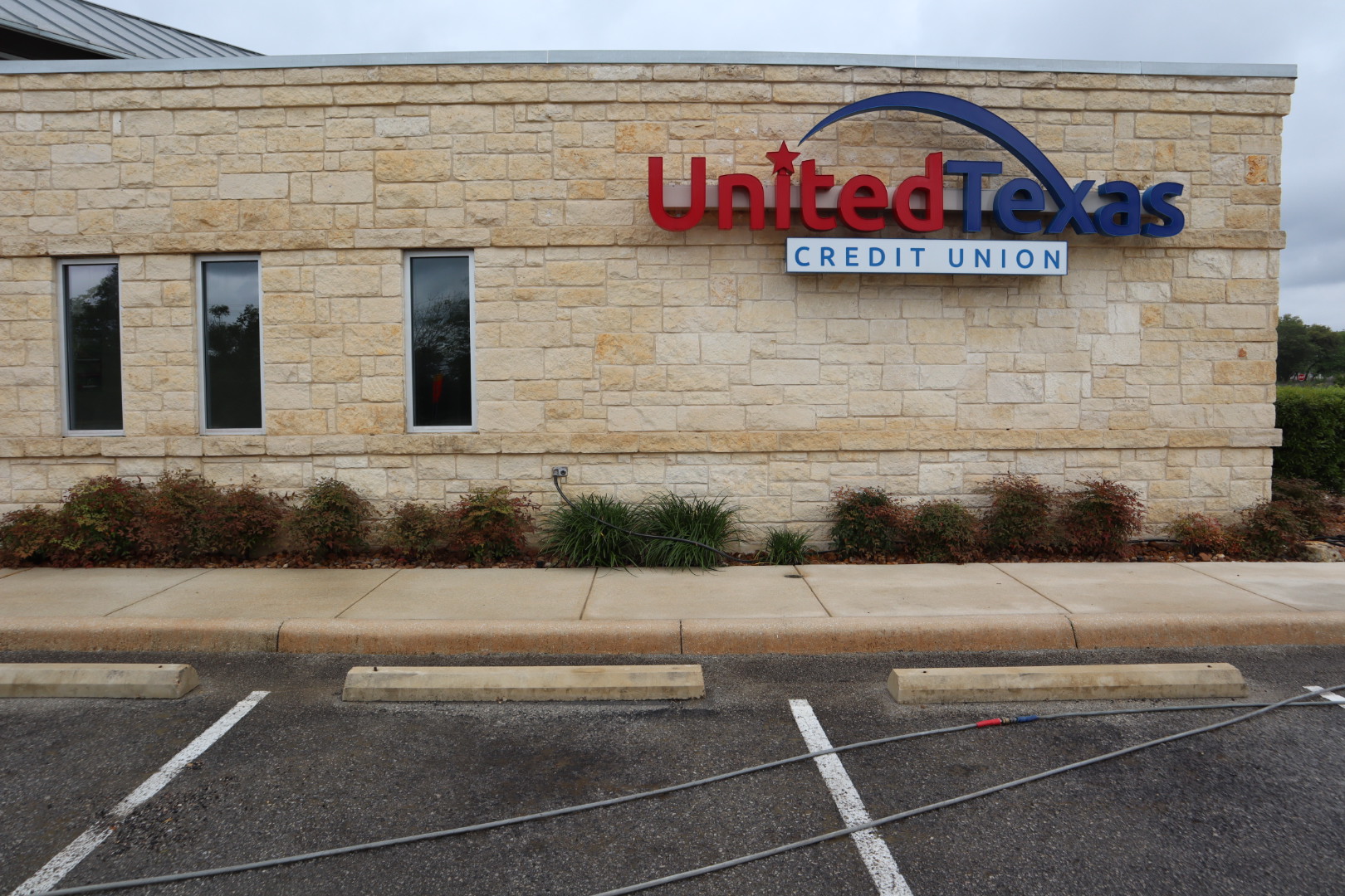 Side of the credit union after cleaning, showing the United Texas Credit Union sign and clean limestone above the sidewalk and parking area