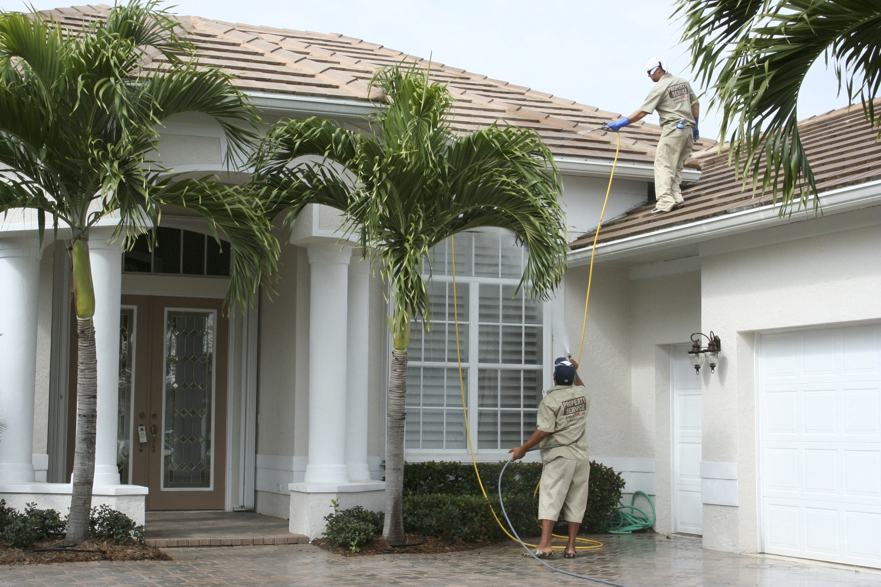 Roof cleaning at Monarch Country Club — Bill Eary on the tile roof running the soft wash while Ralphie works from the ground protecting the plants and managing the hose