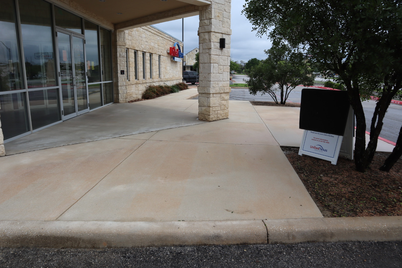 Entry pad and columns at the credit union after cleaning, with the concrete sidewalk restored to a clean, uniform tone