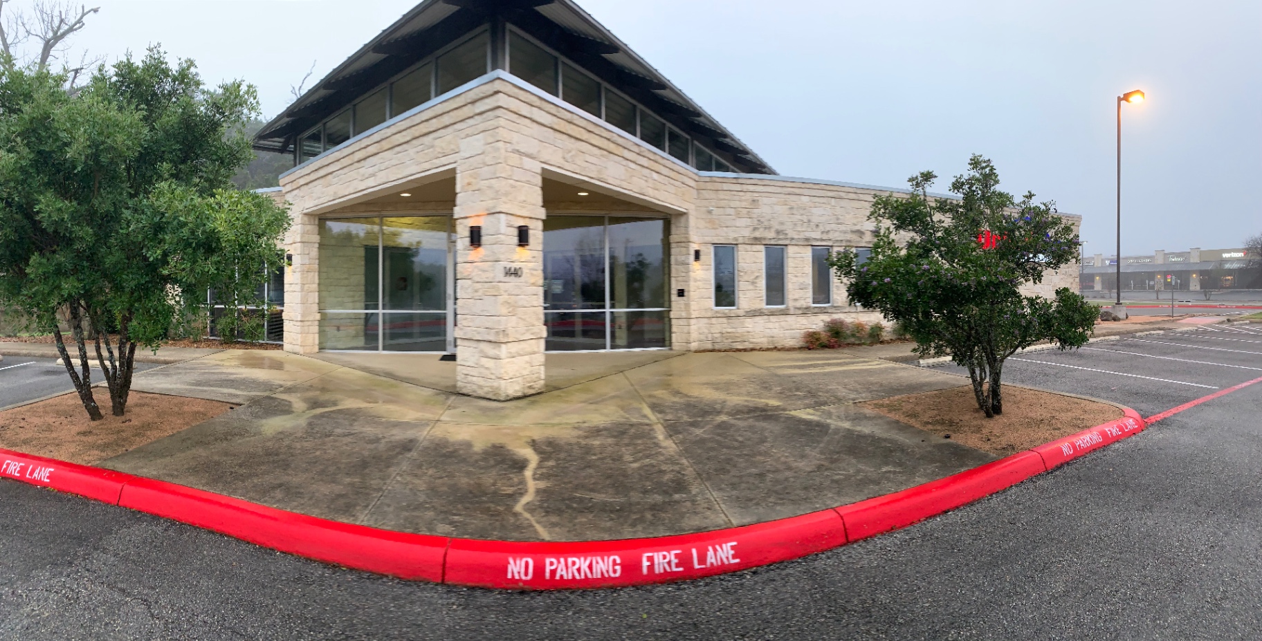 Wide corner view of the credit union building before cleaning, with heavy staining across the concrete walkway inside the fire lane