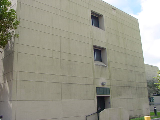 Concrete panel exterior of a building at Miami Children's Hospital before cleaning, with heavy dark streaks, algae staining, and grime running down from the window openings
