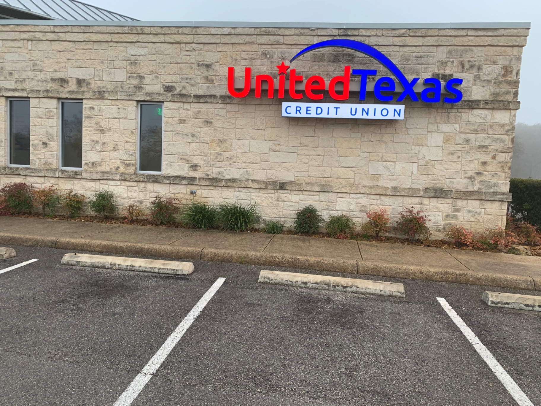 Rear side of the credit union with the United Texas Credit Union sign before cleaning, showing sidewalk stains and darkened stone around the parking area