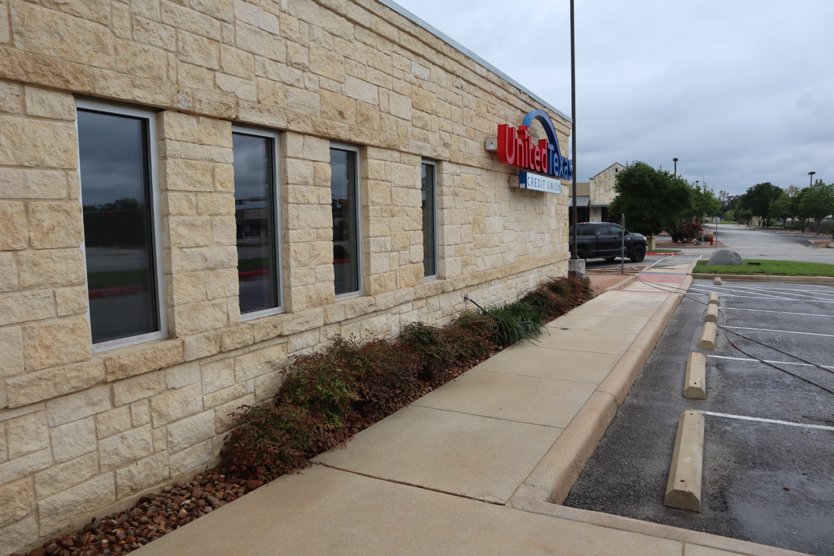 Window wall and sidewalk along the credit union after cleaning, with the limestone bright and even above and below the windows