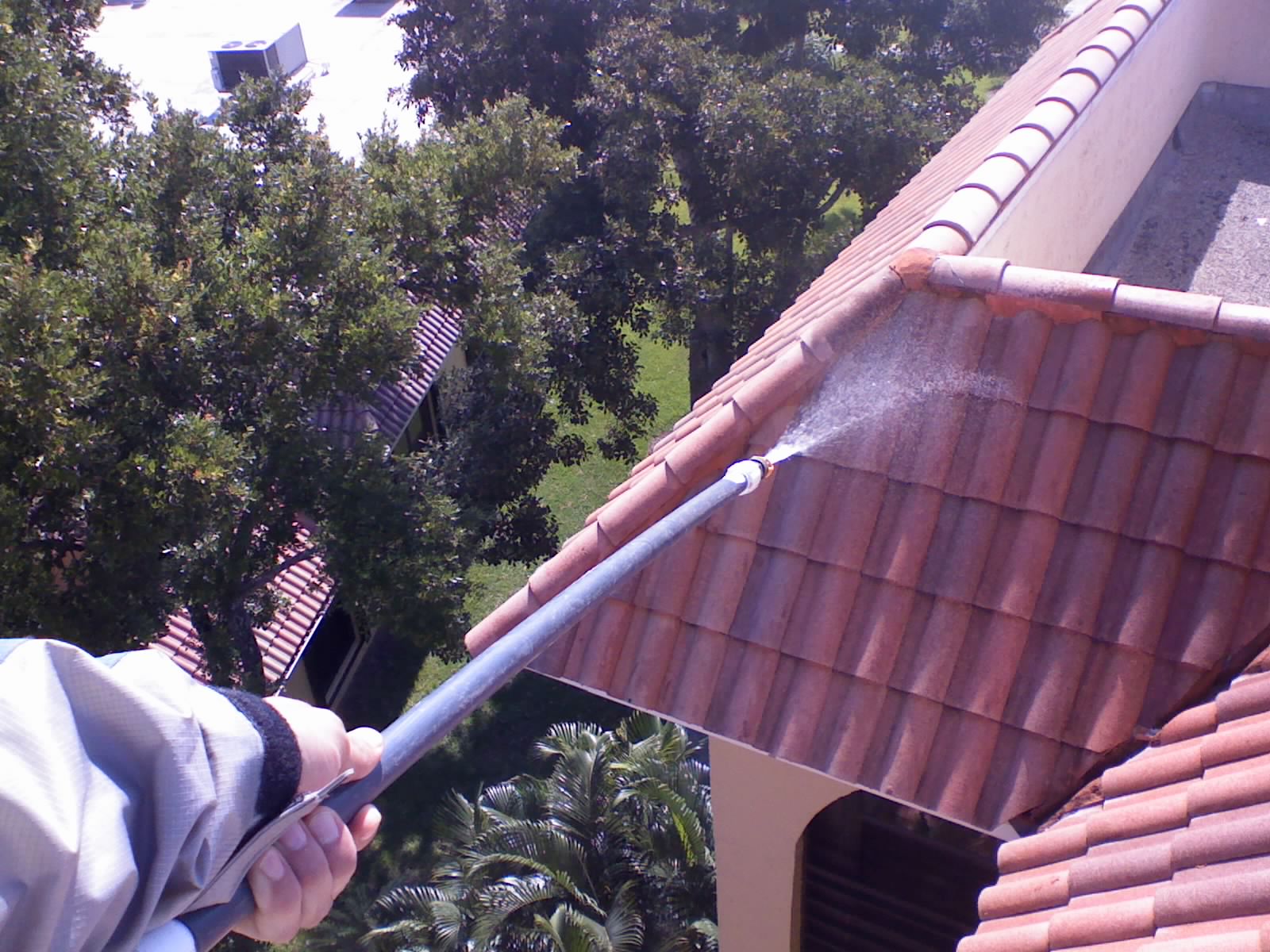 Soft wash roof cleaning wand spraying a fine chemical mist onto a red barrel tile roof at height, gently treating the tile without high pressure