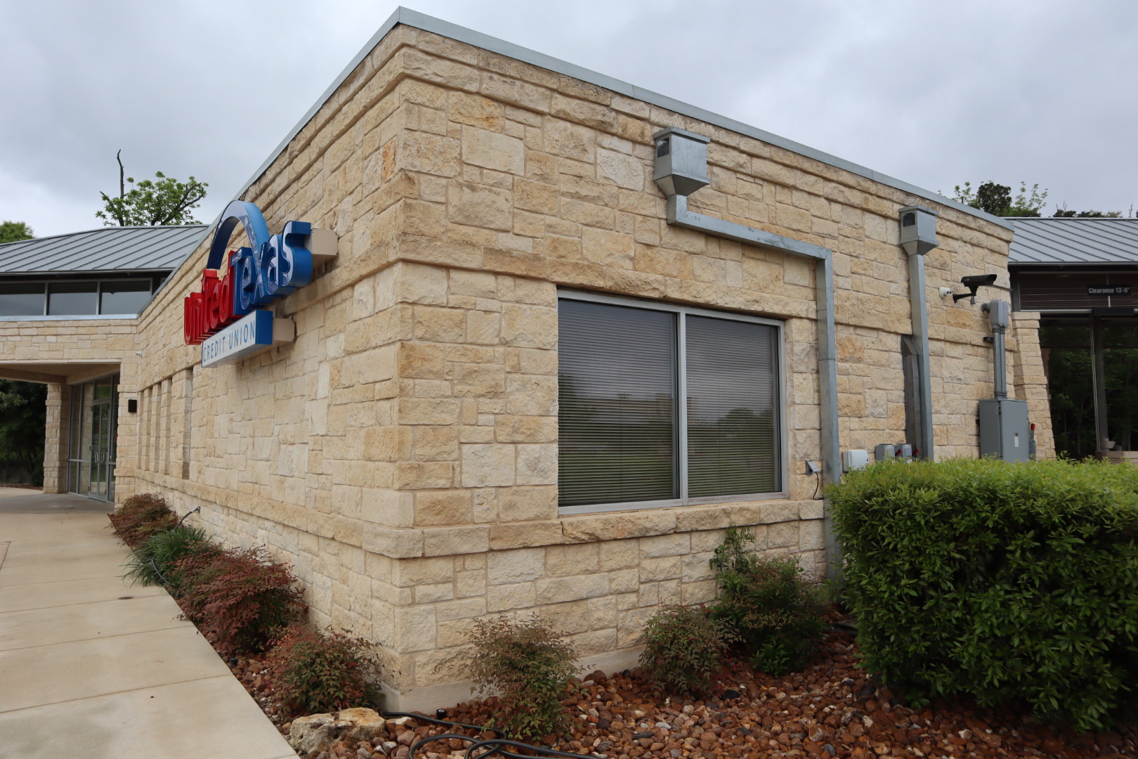 Corner view of the credit union after cleaning, with the stone walls, signage, and window trim restored to a uniform clean finish