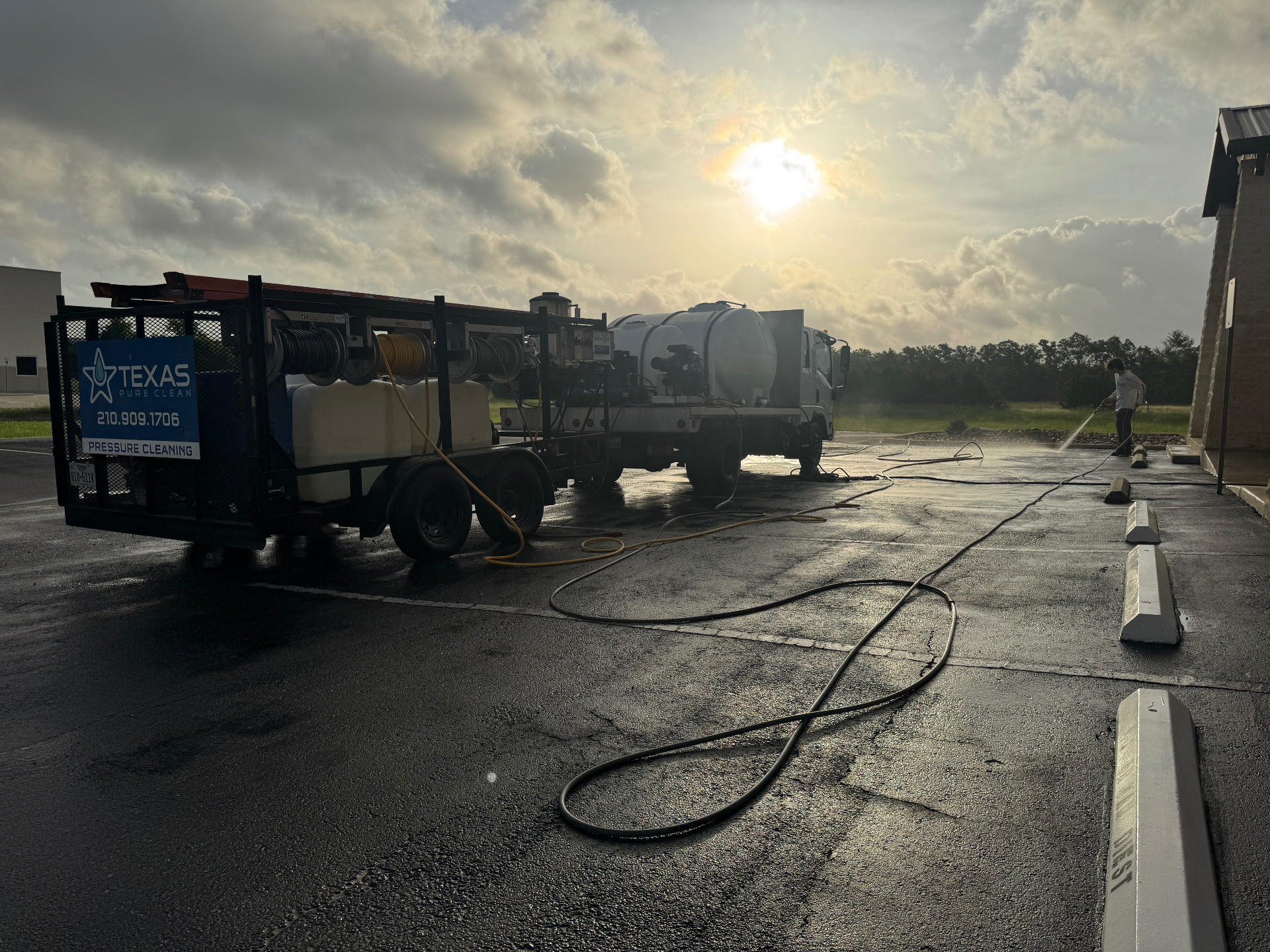 Texas Pure Clean rig and trailer set up on-site at a commercial property, hoses run out and a technician cleaning the flatwork