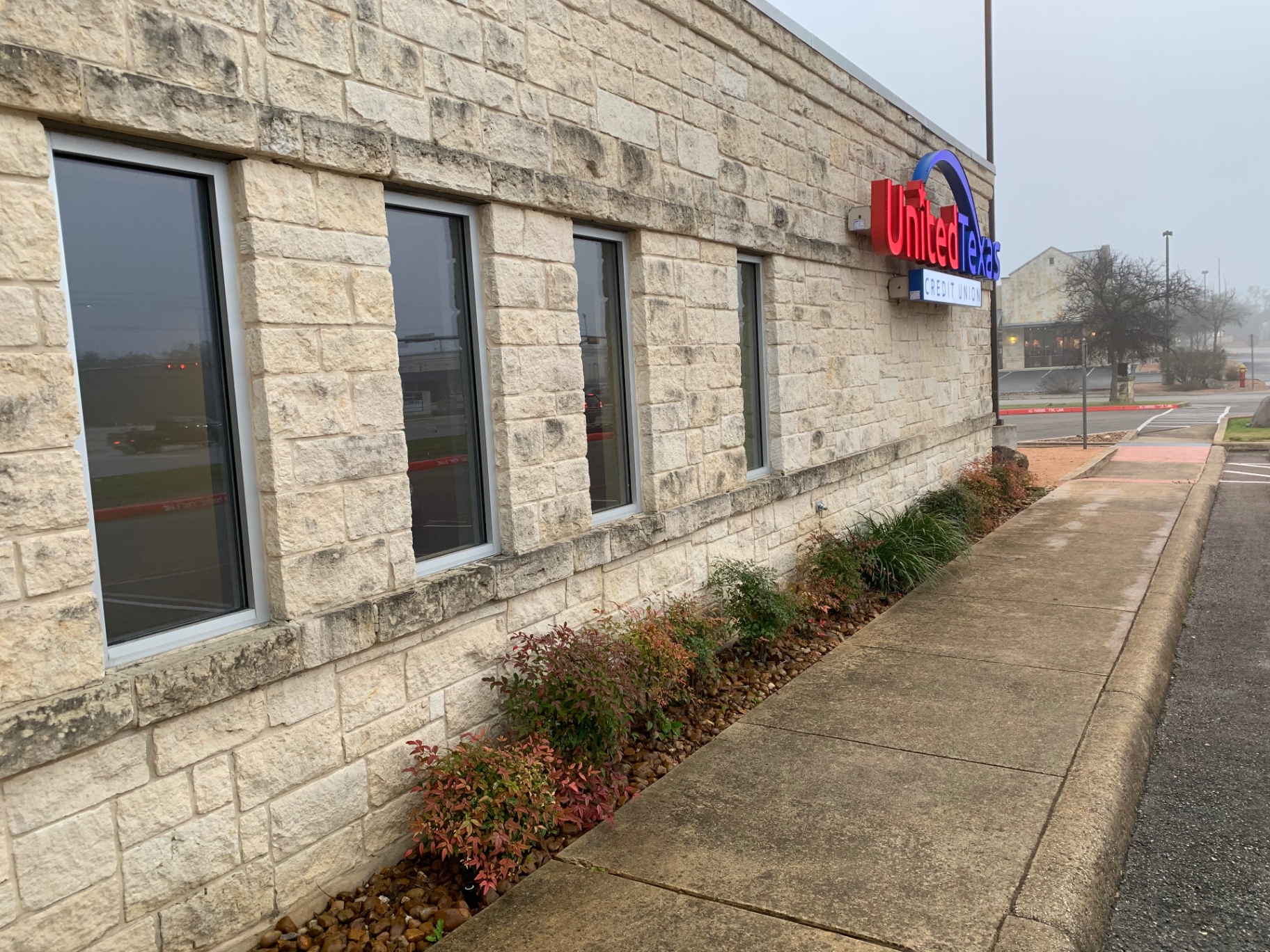Window wall and sidewalk along the credit union before cleaning, with staining running down the limestone above and below the windows