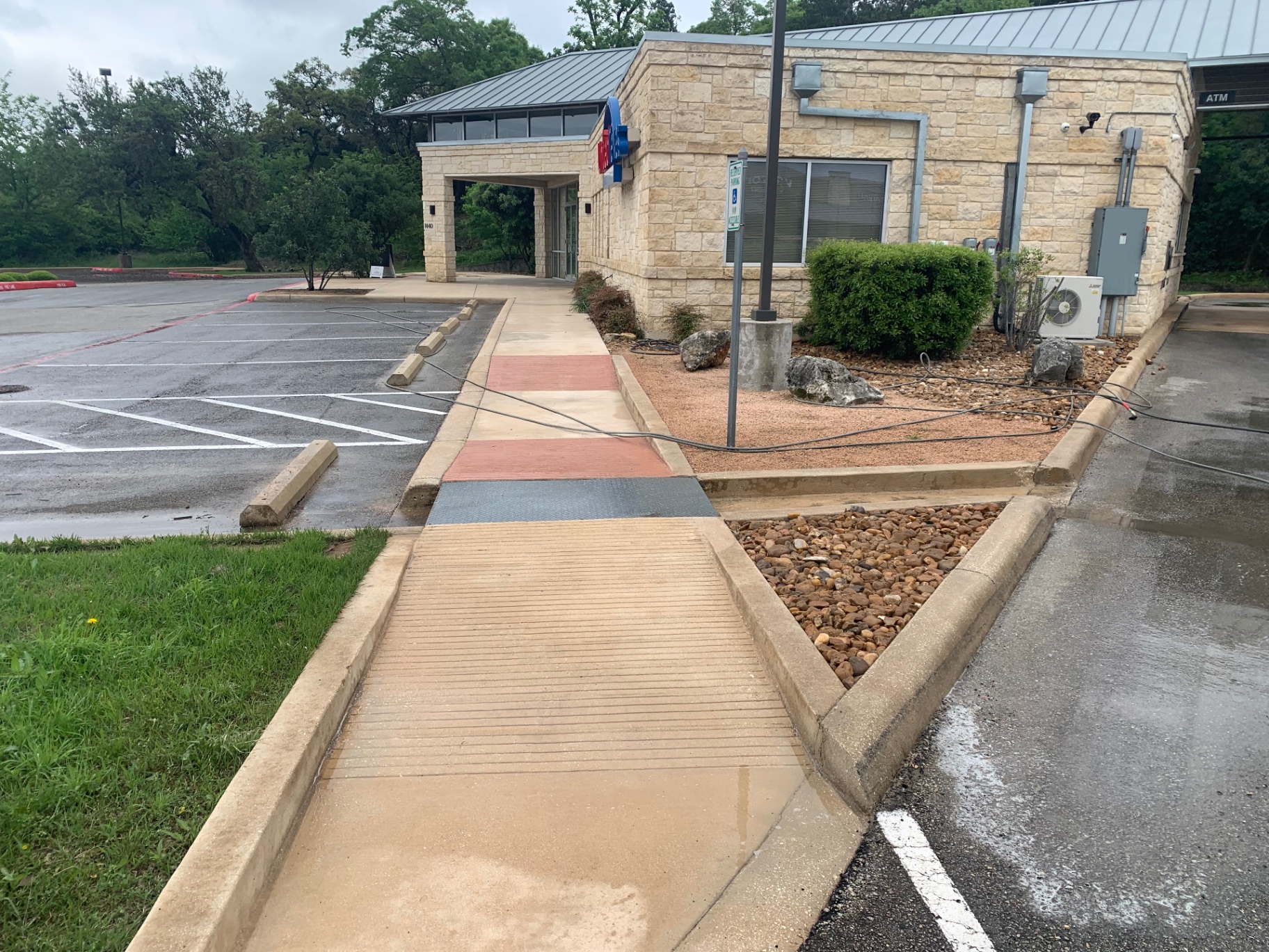 Front entry and ADA walkway at the credit union after cleaning, with the concrete pad, curbs, and stone pillars brought back to a clean, uniform look