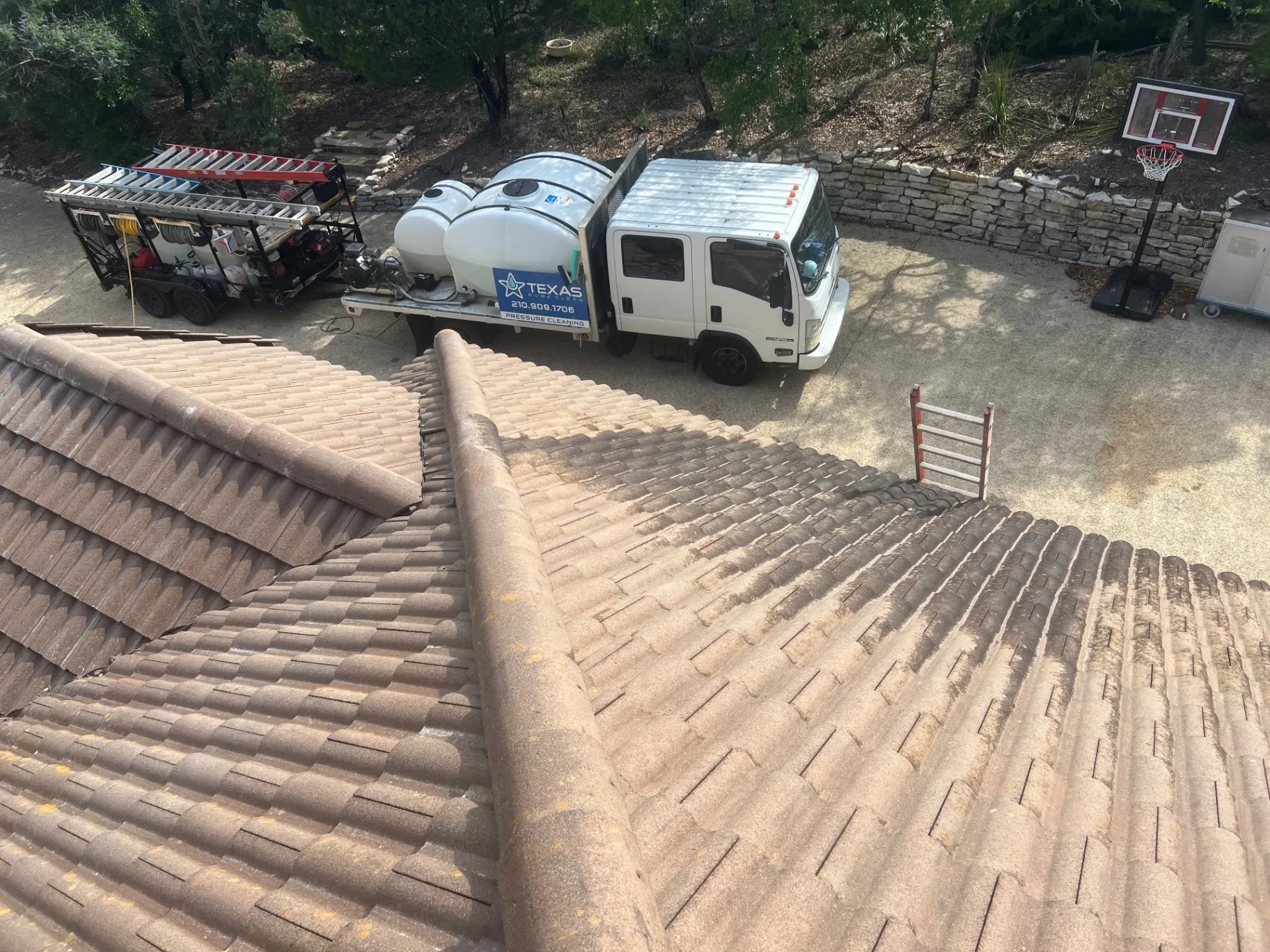 Tile roof during soft wash cleaning showing a sharp contrast between the clean treated section and the dark untreated algae-covered section